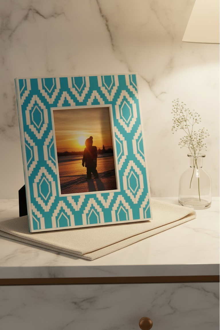 Teal and white patterned photo frame on a marble surface with a sunset silhouette inside.